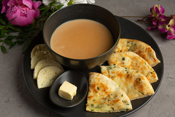 Kalmyk tea in a cup, feta cheese, a pie with herbs and a slice of butter in a black plate