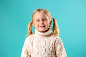 little blonde girl smiling in white knitted sweater on blue background