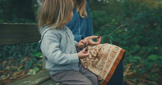 Little toddler sharing chocolate bar with his mother on park bench