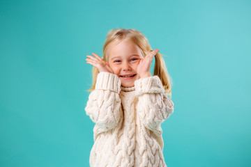 little blonde girl smiling in white knitted sweater on blue background