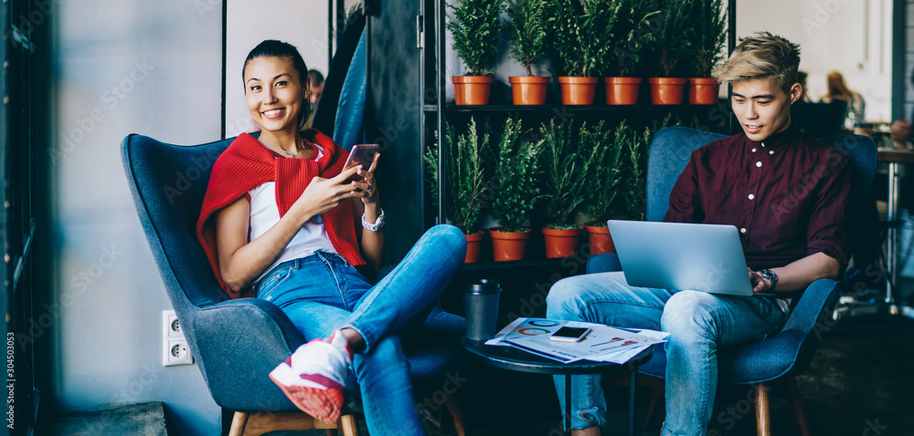 Aufkleber portrait of cheerful cinese hipster blogger smiling at camera while chatting in social networks on s