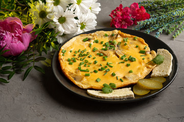 omelet with mushrooms and herbs with cheese and pickles in a black plate
