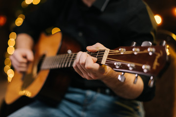 Guy plays guitar close-up. Against the background of a decorated Christmas tree with a garland