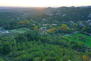 Fototapeta premium Sunset view of the Alpilles valley with green olive tree groves below the historic fortified village Les-Baux-de-Provence, in Bouches du Rhone, Provence, France.