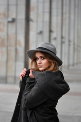 Portrait of beautiful woman with blond hair wearing hat and gray coat. Outdoor portrait in city