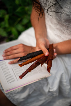Young girl holding tklapi dried mashed fruit candy pastille pulp. Colorful leather from apricot, kiwi, dogwood, strawberry. Cuisine roll up snack. Grapes, dates, lemon, orange, raspberries. Board.