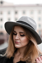 Portrait of beautiful woman with blond hair wearing hat and gray coat. Outdoor portrait in city