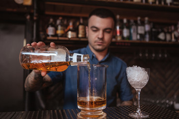 Handsome tattooed young bartender making whiskey based drink for a customer
