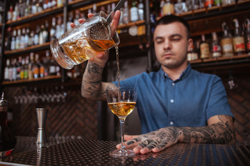 Selective focus on a glass, bartender pouring mixed cocktail into. Profession, entertainment concept