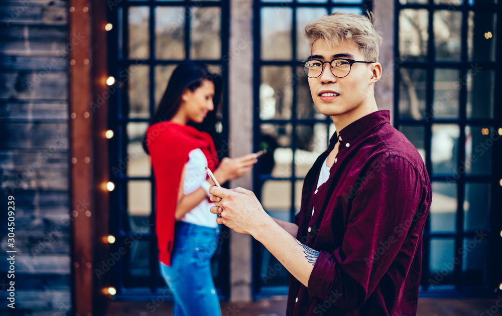 Poster pondering chinese hipster guy in eyeglasses looking away while messaging on smartphone and using 4g 