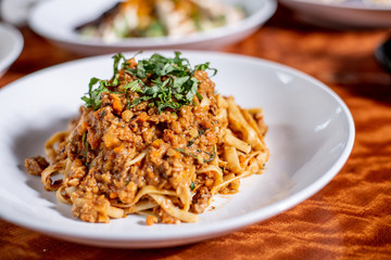 Bolognese handmade spaghetti topped with fresh basil in a white bowl on wood table