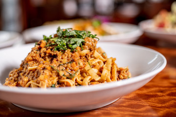 Bolognese handmade spaghetti topped with fresh basil in a white bowl on wood table