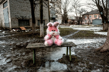 pink plush rabbit sits on a bench in a poor residential area