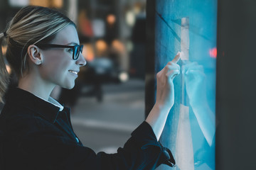 Smiling female standing at big display with advanced digital technology. Young woman touching with...