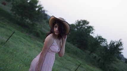 Beautiful woman sitting on a fence staring down at the ground with her hands on her hat