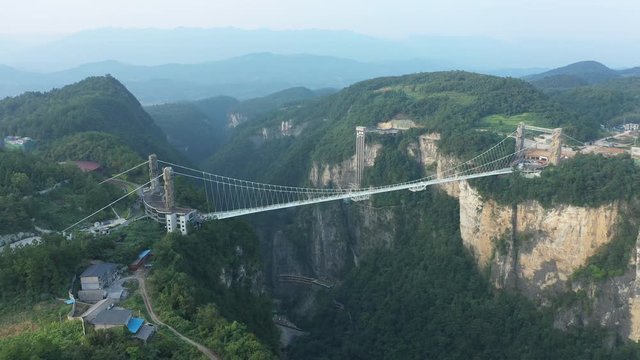 Retreating aerial footage of glass suspension bridge in Zhangjiajie, spanning 430 meters across beautiful mountain valley in central China