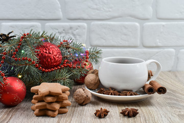 White cup with black tea on the christmas tree phoenias on a wooden table. Red balls. Vanilla, nuts, anise. Spicy cookies.