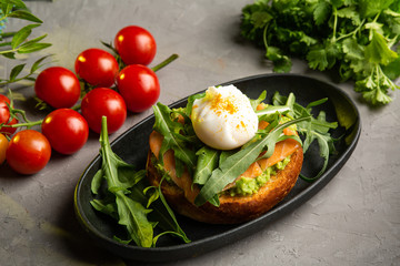 bruschetta salmon with avocado - salted salmon with guacamole, arugula and poached egg on a warm fried bun