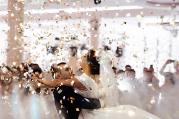 Handsome wedding dance with confetti. Gorgeous stylish happy bride and groom performing their emotional first dance, wedding in a restaurant. Creative couple dancing their first dance