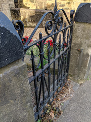 Vintage wrought iron garden gate, painted black. Hung on sandstone gateposts. Gate slightly ajar, with some flowers and leaves.