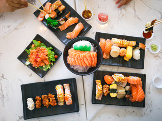 Top view of japanese traditional food A set of sushi rolls on a table in a restaurant , hand of people eating sushi rolls using bamboo sticks.
