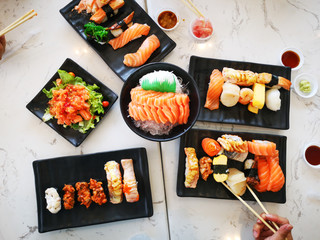 Top view of japanese traditional food A set of sushi rolls on a table in a restaurant , hand of people eating sushi rolls using bamboo sticks.