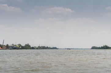 Cai Be, Mekong Delta, Vietnam - March 13, 2019: The wide Mekong River outside town with green belt shoreline under blue and silver cloudscape.
