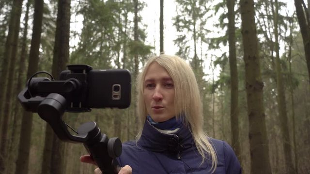 Woman blogger makes video with her phone and gimbal in the forest on nature. She cries and upset tells her viewers and followers on Instagram and YouTube.