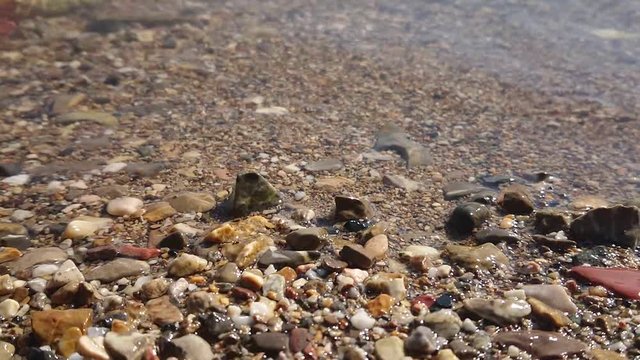 Super slow motion wave at beach with pebbles closeup