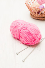 a skein of pink knitting threads with glitter, knitting needles, gray background, basket with threads