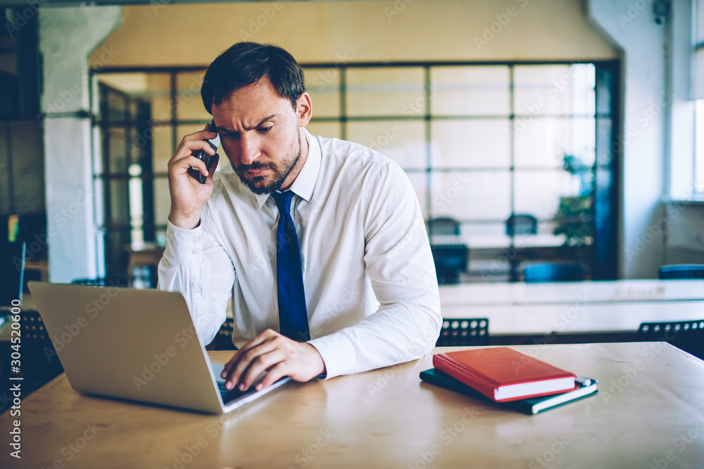Poster serious businessman feeling puzzled with problem during downloading file on laptop computer calling 