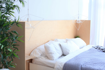  Modern bed with white pillows, a wooden headboard, diamond-shaped lamps and a green palm tree