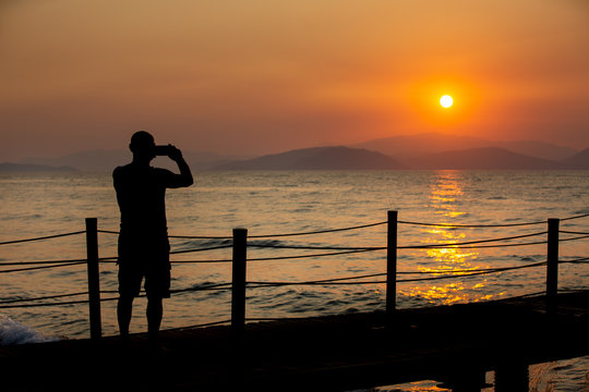 silhouette of man that take  a pictures of sunset on his mobile phone.
