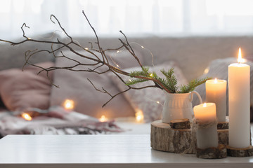 Composition of candles on  white table against the background of  sofa with plaids and pillows....
