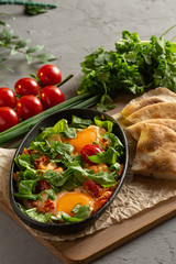 fried eggs with tomatoes and herbs in an oval black dish