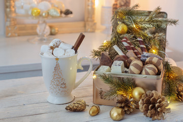 Christmas sweets in golden box and cocoa mug with marshmallows on a white table