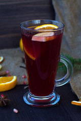 glass of mulled wine with slices of orange, apple and spices, cinnamon and anise star on a wooden table with winter decorations. vertical. hot drinks of winter and autumn. 