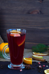 glass of mulled wine with slices of orange, apple and spices, cinnamon and anise star on a wooden background with winter decorations. hot drinks of winter and autumn. vertical