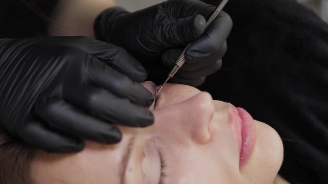 A professional beautician in a beauty salon performs eyelash lamination procedure.