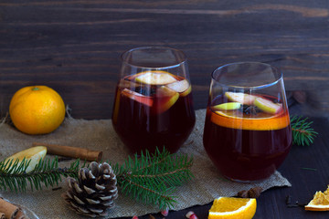 two glasses of red mulled wine with orange, apple and spices on a wooden table with winter...