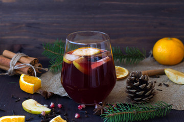 Winter still life. Glass of red hot mulled wine in the centre with apple and spices with sticks...