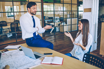 Cheerful male and female business partners enjoying live communication during break form work, positive professional man and woman dressed in formal wear talking to each other near office desktop