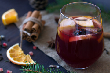 Hot mulled wine in a glass on a wooden background with apple and orange slices and spices with cinnamon. winter and autumn hot drinks. christmas still life with candle and decorations