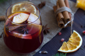 Glass of red hot mulled wine with apple and spices with sticks cinnamon on a wooden table with slices of orange and burlap. Winter and autumn hot drinks.