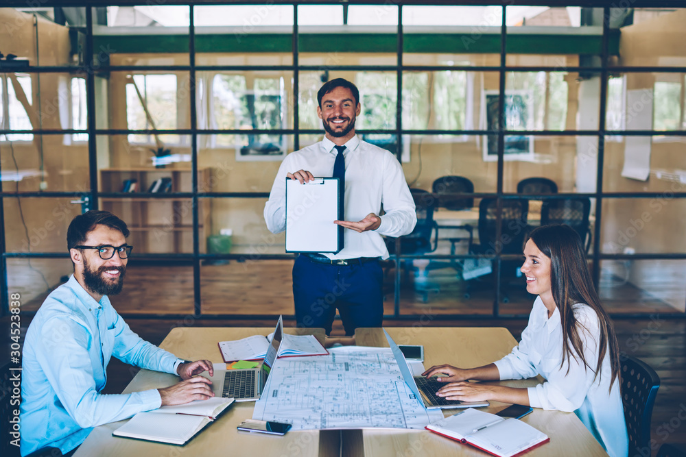 Aufkleber positive man standing near desktop and showing on paper folder discussing information with successfu