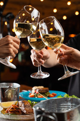 People clink glasses with white wine above a table full of meals in a restaurant