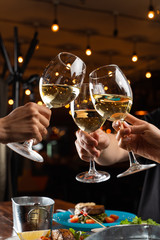 People clink glasses with white wine above a table full of meals in a restaurant