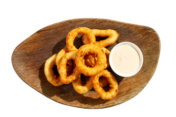Appetizing fried squid rings with sauce on a wooden board. Top view. Isolated over white background.