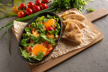 fried eggs with tomatoes and herbs in an oval black dish