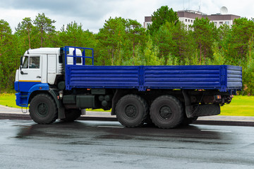An onboard lorry with an elongated blue body and  white cab stands on  road in city in Siberia. Side view. 
